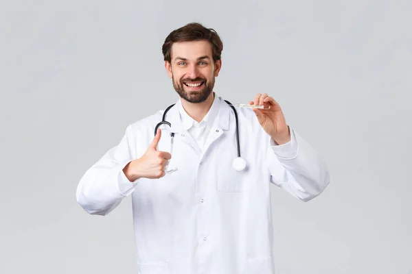 Krankenhaus, medizinisches Personal, covid-19 Behandlungskonzept. Schöner freundlicher Arzt in weißem Peeling, mit Stethoskop, das Daumen nach oben zeigt, um die Temperatur des Patienten zu messen, Thermometer zeigen — Stockfoto