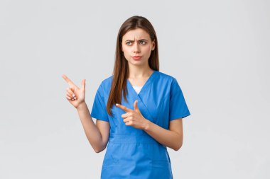 Sağlık çalışanları, virüsü, sigortayı ve ilaç konseptini engelleyin. Bir sorun var. Ciddi derecede hoşnutsuz hemşire ya da doktor mavi önlüklü, somurtkan bakışlı ve endişeli sol işaret