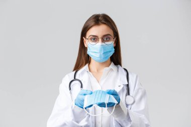 Covid-19, virüsü önleme, klinik, sağlık çalışanları ve karantina konsepti. Tıbbi maskeli, eldivenli, beyaz önlüklü, hastalara yüz maskesi koruması yapan genç doktor, ciddi görün.