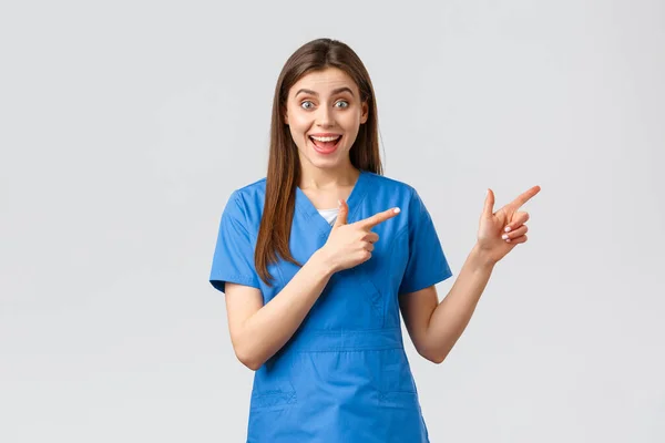 医療従事者,ウイルスを防止します,保険や医療の概念.右の指を指して青いスクラブで興奮した幸せな女性看護師や医師,面白い見て,プロモーションや良いニュースについての情報 — ストック写真