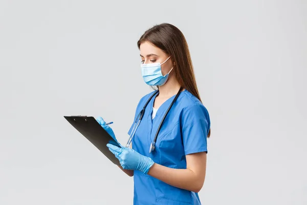 Covid-19, preventing virus, health, healthcare workers and quarantine concept. Professional serious female nurse or doctor during regular patient checkup, writing down info on clipboard — Stock Photo, Image