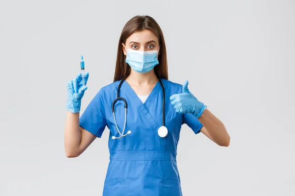 Covid-19, prevence viru, zdravotnických pracovníků a koncepce karantény. Sebevědomá ošetřovatelka, doktorka v modrých pláštích, lékařská maska a rukavice zaručují kvalitu koronavirové vakcíny, držte stříkačku — Stock fotografie