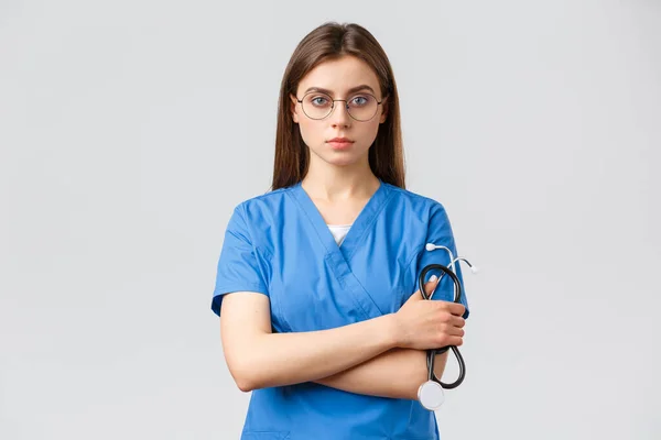 Pracownicy służby zdrowia, medycyna, ubezpieczenie i koncepcja pandemii covid-19. Poważny i zdecydowany, profesjonalna pielęgniarka, lekarz w niebieskim fartuchu, trzymając stetoskop, nosić okulary, wyglądać pewnie — Zdjęcie stockowe