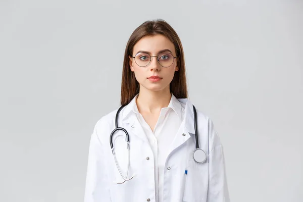 Healthcare workers, medicine, insurance and covid-19 pandemic concept. Serious-looking smart professional doctor, nurse in white scrubs and stethoscope, look camera determined, grey background — Stock Photo, Image