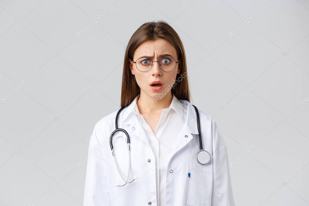 Healthcare workers, medicine, insurance and covid-19 pandemic concept. Shocked nervous female doctor in white scrubs and glasses, doctor gasping and staring concerned camera