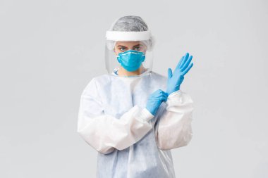 Covid-19, virüsün önlenmesi, sağlık, sağlık çalışanları ve karantina konsepti. Kişisel koruma ekipmanları içinde ciddi bir kadın doktor PPE, kalkan, yüz maskesi takıp hasta odasına giriyor.