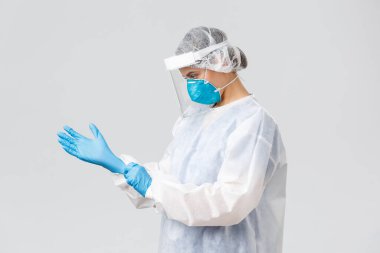 Covid-19, virüsün önlenmesi, sağlık, sağlık çalışanları ve karantina konsepti. Kişisel koruyucu ekipman içinde genç bir doktor, hemşire Coronavirus hastasıyla çalışmak için lastik eldiven taktı.