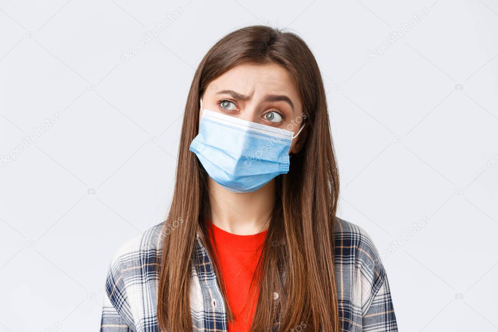 Coronavirus outbreak, leisure on quarantine, social distancing and emotions concept. Thoughtful and intrigued woman in medical mask, looking left with interest, thinking, white background