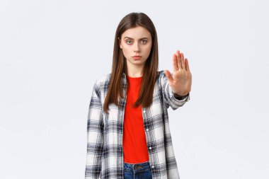 Yaşam tarzı, farklı duygular, boş zaman aktiviteleri konsepti. Durma zamanı. Sıradan giyinmiş ciddi bir genç kadın, yasaklamak, yasaklamak ya da yasaklamak için elini uzat, beyaz arka plan.
