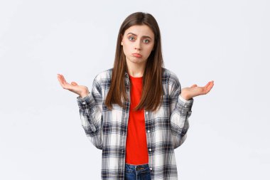 Yaşam tarzı, farklı duygular, boş zaman aktiviteleri konsepti. İsteksiz ve dikkatsiz genç bir kadın ellerini yana açmış omuz silkiyor, bilmiyorum, yardım edemiyorum, hiçbir fikrim yok, beyaz arka planda duruyorum.
