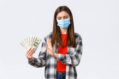 Para transferi, yatırım, covid-19 salgını ve ev konseptinden çalışma. Tıbbi maskeli hoşnutsuz bir kız rüşvet olarak nakit kabul etmiyor, dolar işareti göstermiyor ve kaşlarını çatıyor.