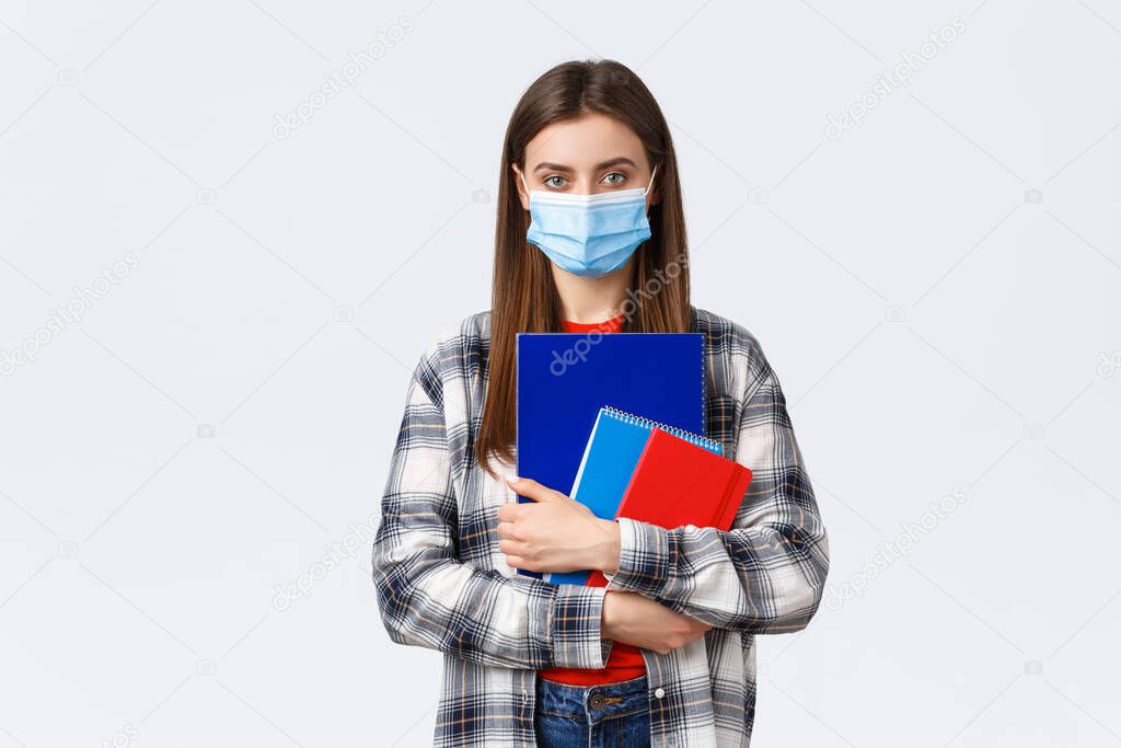 Coronavirus pandemic, covid-19 education, and back to school concept. Young female student in medical mask holding notebooks, going to class, freshman in university in personal protective facemask