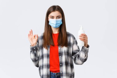 Coronavirus salgını, karantina, sosyal mesafeler ve duygu kavramı. Kendine güvenen tıbbi maskeli genç bir kadın el sabunu ya da dezenfektan tavsiye ediyor.