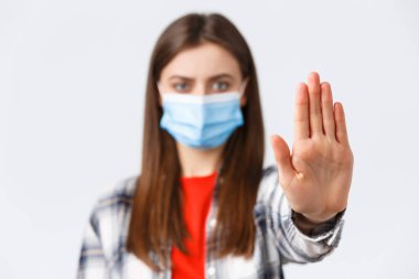 Coronavirus salgını, karantina, sosyal mesafeler ve duygu kavramı. Ciddi bir kadın, dur demek için avuç içini uzatır, kötü kararlar almaktan men eder, tıbbi maske takar.