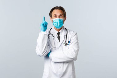 Covid-19, virüsü önleme, sağlık çalışanları ve aşı konsepti. Tıbbi maskeli ve eldivenli heyecanlı erkek doktorun Coronavirüs hastalarıyla ilgili önerileri var, parmağını kaldır.