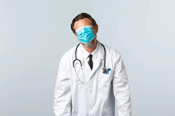 Covid-19, virüsü önleme, sağlık çalışanları ve aşı konsepti. İsteksiz ve yorgun doktor maskeyi bütün yüzünden çeker ve yorgun düşmüş, beyaz arka planda durur. — Stok fotoğraf