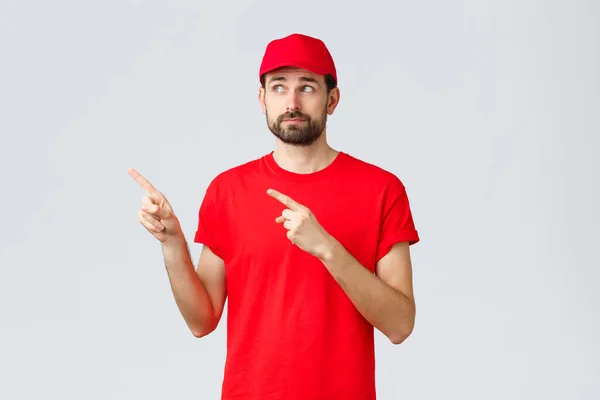 オンラインショッピング、隔離中の配達とテイクアウトの概念。赤のTシャツと帽子を着た従業員は失望した指を左上隅に向ける — ストック写真