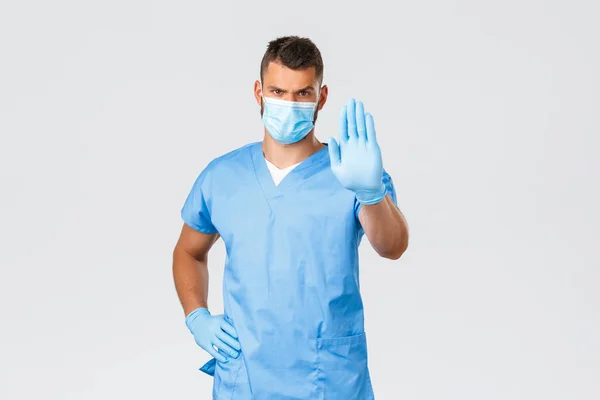 医療従事者, covid-19,コロナウイルスやウイルスの概念を防止.真剣に見て自信がありハンサムな医者は、患者の停止を求めて、医療用マスクと手袋を着用し、家庭の自己隔離を教えてください — ストック写真