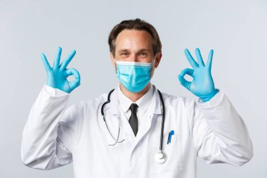 Covid-19, virüs, sağlık ve aşı konsepti. Doktor, klinikteki hizmetin kalitesini garanti eder ve garanti eder. Hastalar hastane çalışanlarına güvenebilir. Maskeli doktor ve eldivenler tamam işareti gösteriyor.