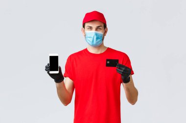 Bağlantı kurulamayan teslimat, ödeme ve kovid 19 sırasında online alışveriş, kendini karantina. Kırmızı üniformalı gülümseyen kurye, eldivenler ve yüz maskesi akıllı telefon ekranı ve kredi kartı, siparişler için uygulama