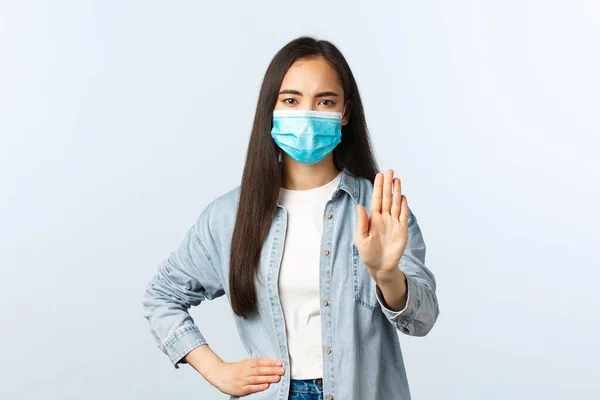 Social distanslivsstil, covid-19 pandemisk vardag och fritidskoncept. Allvarligt utseende asiatisk flicka visa stopp gest, hålla avstånd under coronavirus, bära medicinsk mask — Stockfoto