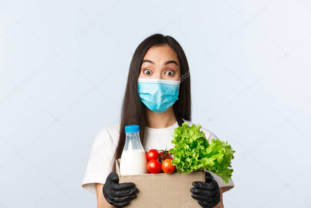 Covid-19, grocery store, employment, small business an preventing virus concept. Cheerful cute asian shop employee, cashier in medical mask and gloves giving client takeaway order