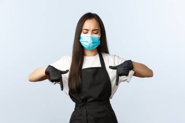 Covid-19 salgını, sosyal mesafeler, küçük işletmeler ve virüs konseptini önlemek. Şüpheci ve şüpheci Asyalı barista, tıbbi maskeli ve eldivenli bayan kahveci üzgün.