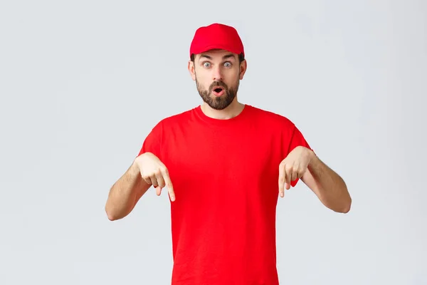 Nätshopping, leverans under karantän- och hämtningskoncept. Förvånad och fascinerad kurir informera kunder, anställd i röd uniform mössa och t-shirt pekar finger ner, säg wow — Stockfoto