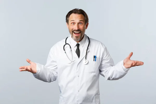 Covid-19, coronavirus outbreak, healthcare workers and pandemic concept. Surprised happy male doctor receive great news, congratulating patient for releasing hospital, white background — Stock Photo, Image