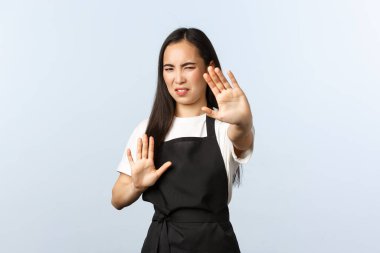 Kahve dükkanı, küçük işletme ve başlangıç konsepti. Rahatsız ve rahatsız olmuş siyah önlüklü Asyalı bayan barista kamera ışığından yüzünü gizlemeye çalışıyor, ateşi kes diyor, savunma pozisyonunda duruyor.