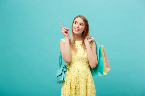 Hermosa joven con bolsa de compras en vestido amarillo apunta a algo con su dedo . — Foto de Stock