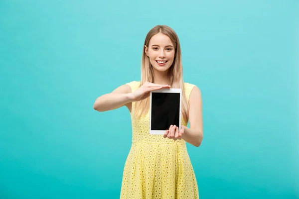 Mujer retrato mostrando la pantalla de la tableta sonriendo usando vestido amarillo aislado sobre fondo azul . — Foto de Stock