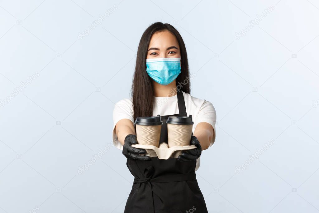 Covid-19, social distancing, small coffee shop business and preventing virus concept. Friendly pleasant asian waitress, cafe barista in medical mask serving coffee, handing order with takeaway cups