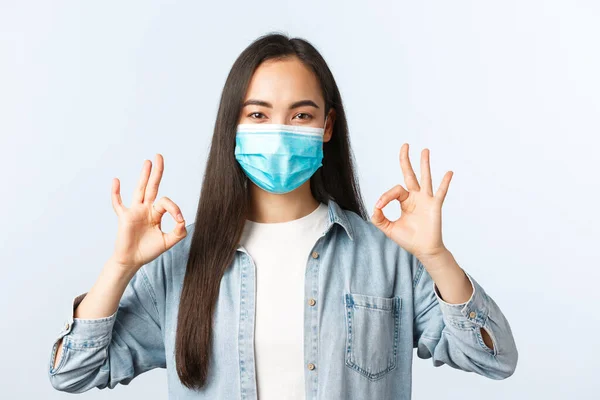 Social distanslivsstil, covid-19 pandemisk vardag och fritidskoncept. Nöjd asiatisk kvinna i medicinsk mask säga inga problem, hålla med eller godkänna kvalitet, visar okej gest glad — Stockfoto