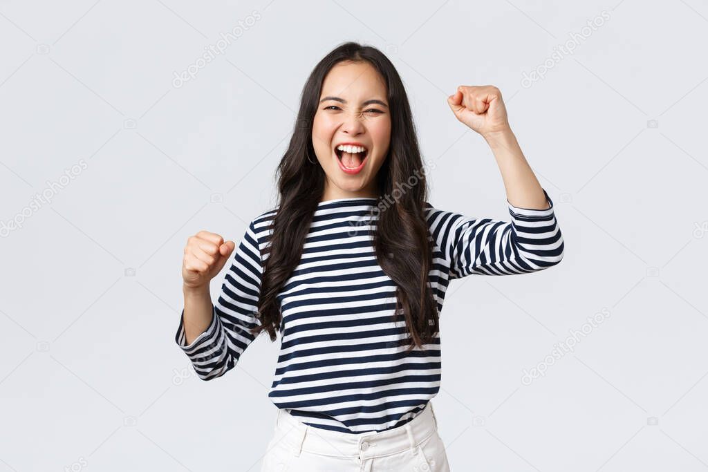 Lifestyle, people emotions and casual concept. Excited happy asian woman attend sport competition, rooting and chanting for team, raising hands up and shout yes supportive