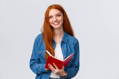 Belden yukarı, sevimli kızıl saçlı genç kız favori üniversite dersinde not alıyor, elinde kalem ve kırmızı defter, gülümseyen kaygısız kamera, bir şeyler yazıyor, yapılacaklar listesi yapıyor.