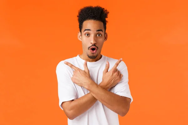 Le type qui regarde un ami demander de l'aide pour acheter des cadeaux. Amusé et excité heureux afro-américain mâle pointant coins supérieur droit et gauche comme tout essayer de faire un choix, fond orange — Photo