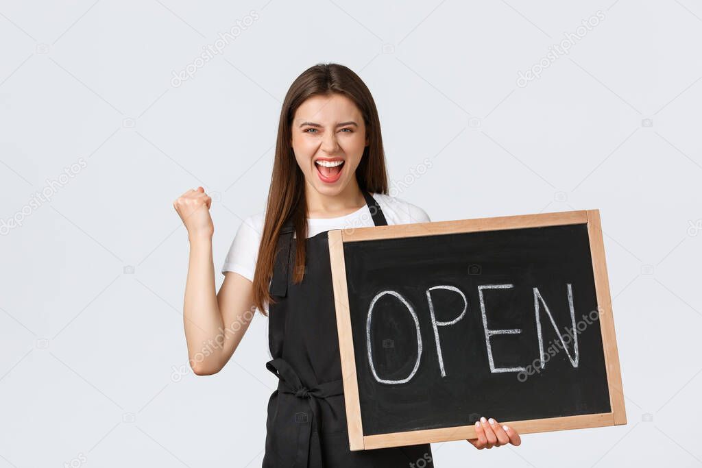 Grocery store employees, small business and coffee shops concept. Rejoicing happy barista in black apron fist pump triumphing that cafe finally open, showing sign, standing white background