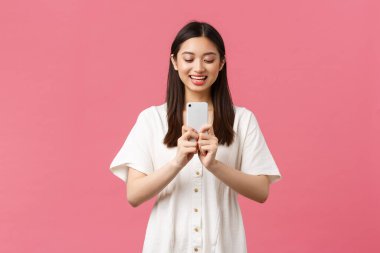 Güzellik, insan duyguları ve teknoloji konsepti. Gülümseyen mutlu Asyalı kadın blogcu, şık kız akıllı telefonda fotoğraf çekiyor, neşeli görünüyor, cep telefonuyla fotoğraf çekiyor.