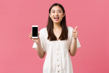Güzellik, insan duyguları ve teknoloji konsepti. Tatmin olmuş mutlu Asyalı kız cep telefonu ekranı uygulamasını göstermek için onay verdi, ayakta duran pembe arka plan uygulaması önerisi