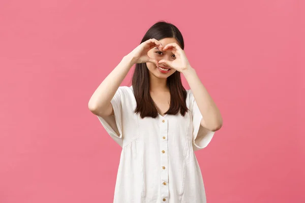Schönheit, Menschen-Emotionen und Sommerfreizeitkonzept. Schöne, romantische schüchterne asiatische Mädchen in weißem Kleid bekennen Sympathie oder Liebe, wie jemand, zeigt Herzzeichen und lächelt über rosa Hintergrund — Stockfoto