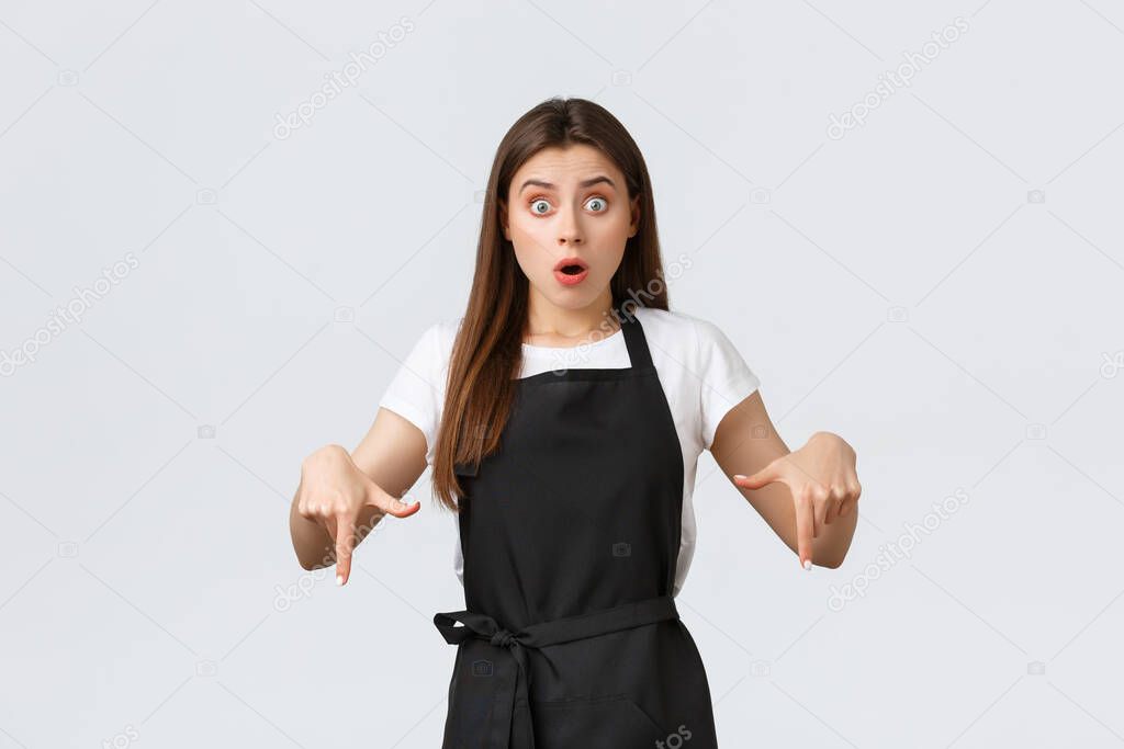 Small business, employees and coffee shop concept. Concerned and shocked waitress pointing fingers down. Gasping confused barista asking question. Astonished saleswoman tell big news