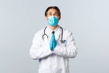 Covid-19, virüsü önleme, sağlık çalışanları ve aşı konsepti. Tıbbi maskeli ve eldivenli ümitsiz doktor Tanrı 'ya yalvarıyor, dua ediyor, yalvarıyor.