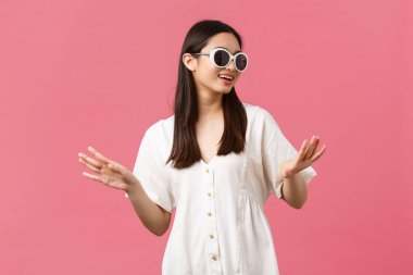 Güzellik, insan duyguları ve yaz tatili konsepti. Şık, mutlu Asyalı turist. Güzellik salonundan sonra eğleniyor. Yeni tırnaklar yaptırıyor, güneş gözlüğü takıyor, pembe arka plan kullanıyor.