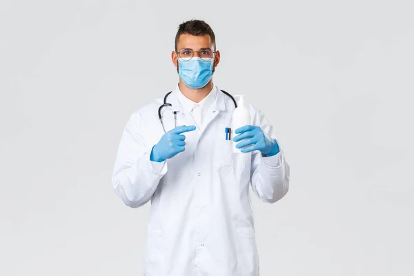 Covid-19, 의료 종사자, 전염병, 그리고 바이러스의 개념 방지. 의료용 마스크와 장갑을 착용하고 있는 라틴 아메리카의 의사, 수술복을 입은 의사는 비누를 추천하면서 손으로 소독제를 가리키고 있다 — 스톡 사진