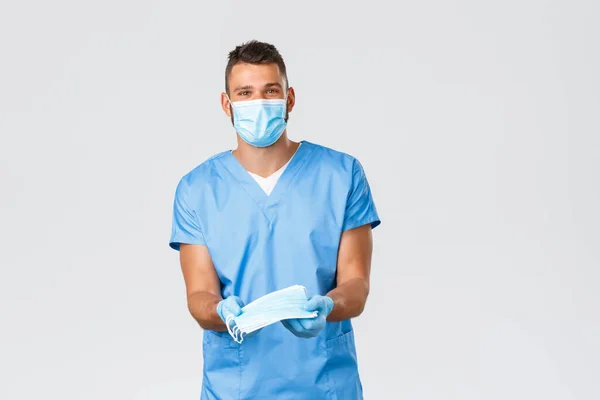 Gezondheidswerkers, covid-19, coronavirus en het voorkomen van virus concept. Vriendelijk knappe arts, lachende verpleegkundige in scrubs en beschermende apparatuur, geef patiënt medische maskers tijdens een pandemie — Stockfoto