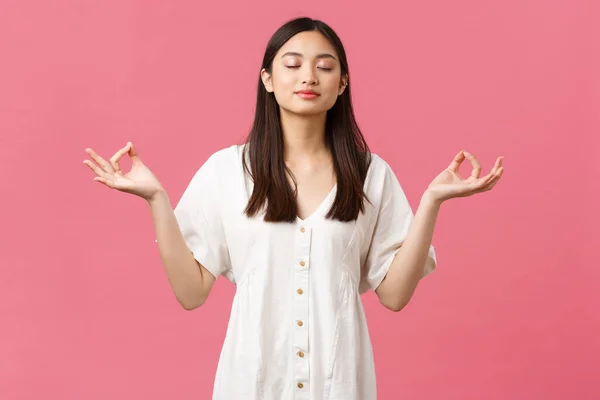 Skönhet, människor känslor och sommar fritid koncept. Avslappnad och lugn, beslutsam ung asiatisk kvinna mediterar i vit klänning, blunda och göra yoga andningsövningar, rosa bakgrund — Stockfoto