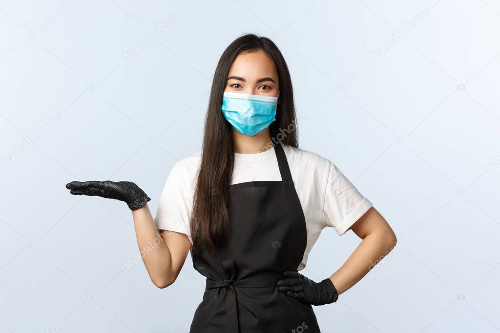 Covid-19, social distancing, small coffee shop business and preventing virus concept. Cute asian restaurant or cafe barista, employee in medical mask and gloves holding product on hand