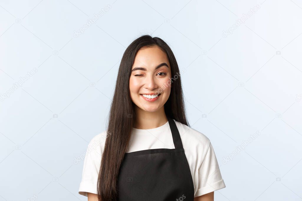 Coffee shop, small business and startup concept. Friendly and cheeky, attractive asian barista, female cafe or shop worker in black apron smiling and wink at client