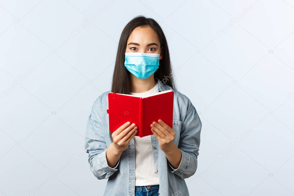Covid-19 pandemic, education during coronavirus, back to school concept. Excited female asian in medical mask read sibling secret diary, look astonished and surprised, studying notes